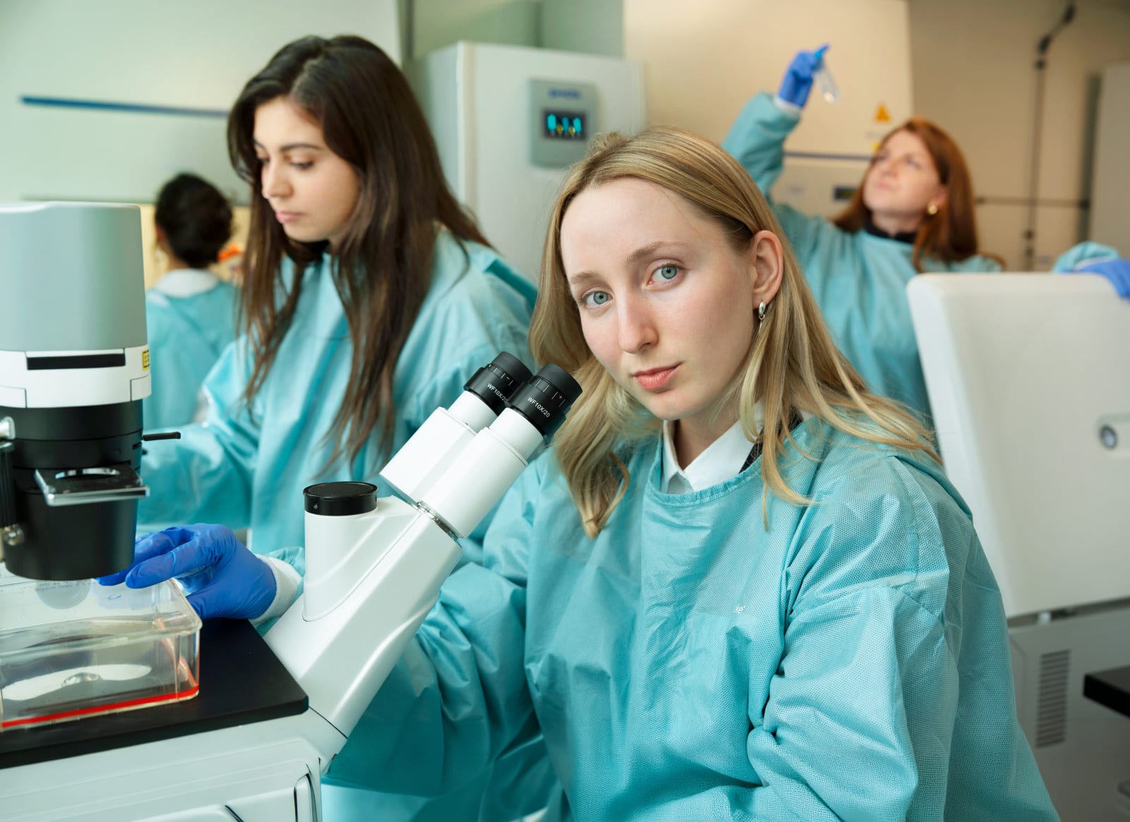 Des chercheuses de Gustave Roussy en blouse dans un laboratoire, l’une d’elles devant un microscope.