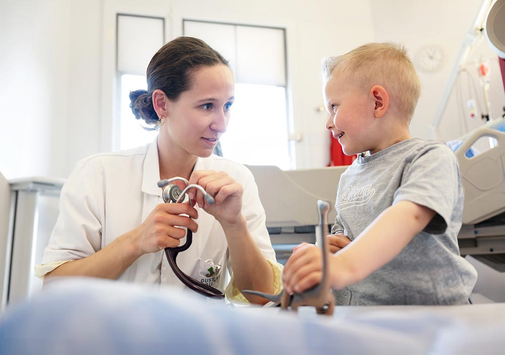 Une infirmière de Gustave Roussy ausculte un jeune patient souriant.